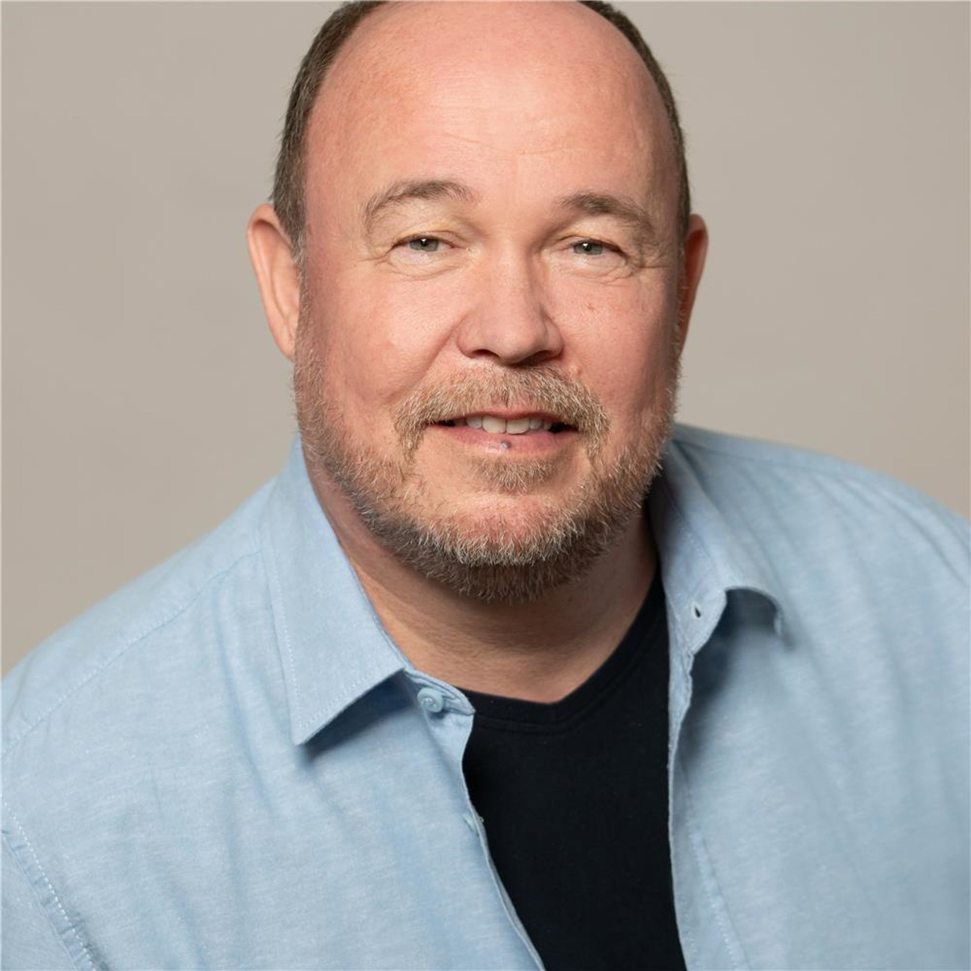 Dietmar Mainz trägt ein hellblaues Hemd über einem schwarzen T-Shirt vor einfarbigem Hintergrund.